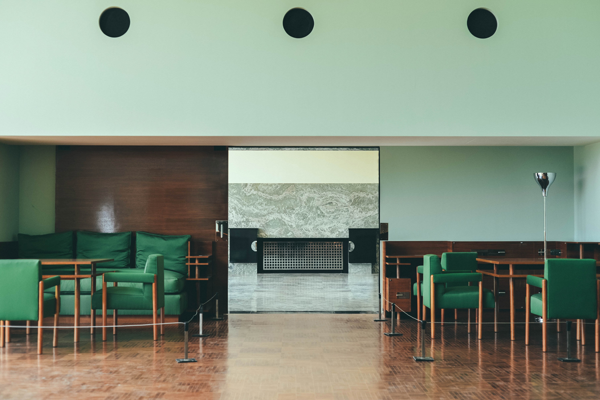 Fotografia de um ambiente interno com sofá e poltronas na cor verde. As paredes são na cor verde-claro