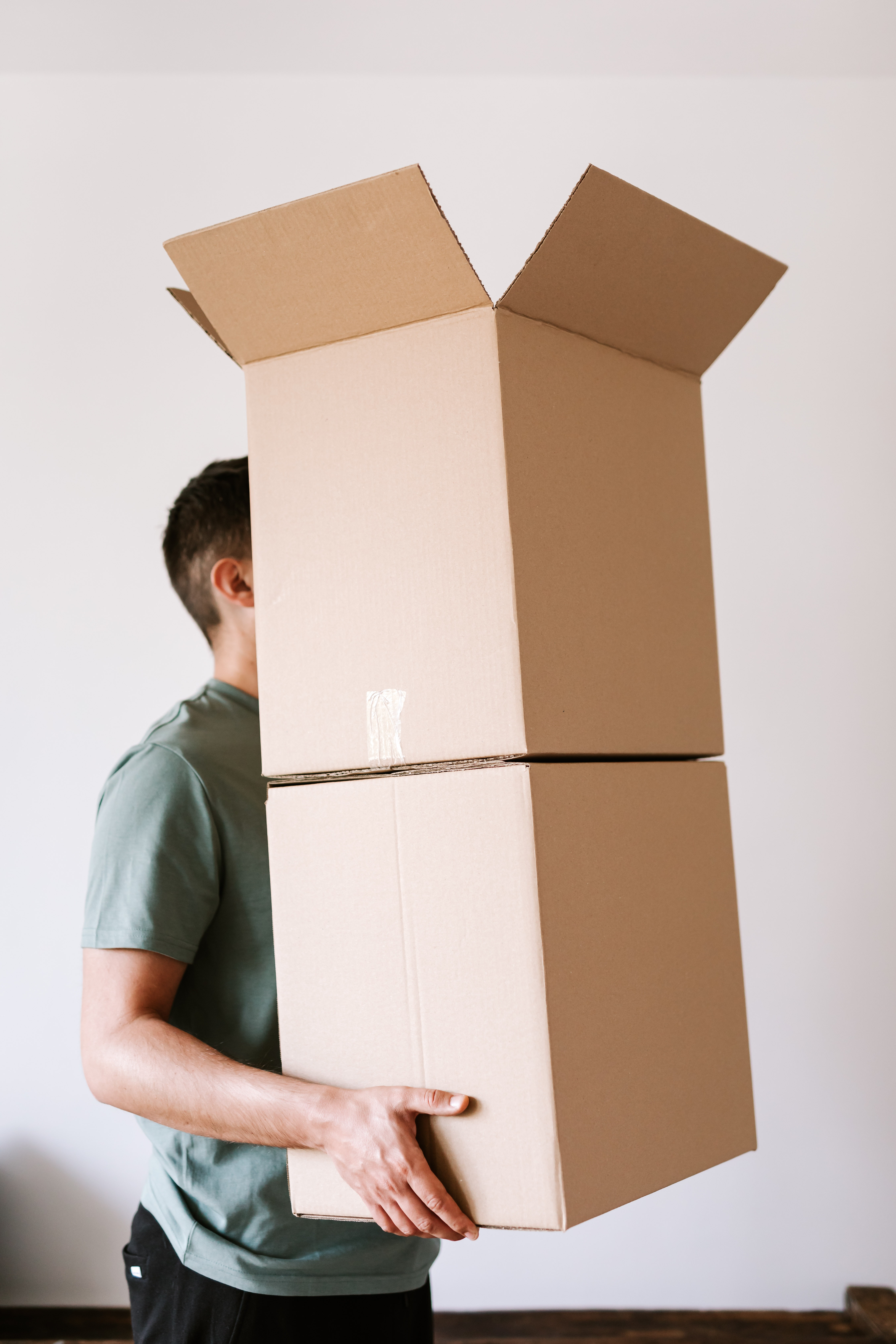 Fotografia de um homem carregando duas caixas de papelão empilhadas.