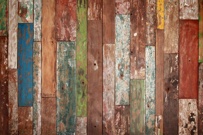 Fotografia de um painel de madeira composto de ripas com a pintura descascada de várias cores (azul, verde, vermelho, amarelo etc.).
