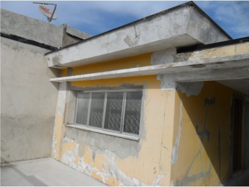 Fotografia de uma fachada de uma casa térrea, com paredes amarelas e apresentando marcas de rachaduras e descascamento de tinta.