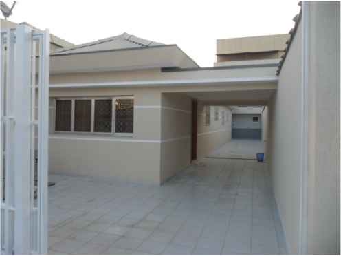 Fotografia da mesma casa apresentada anteriormente, mas agora reformada, com aplicação de textura na cor bege e 2 listras brancas horizontais nas paredes térreas. É possível identificar o telhado também reformado.
