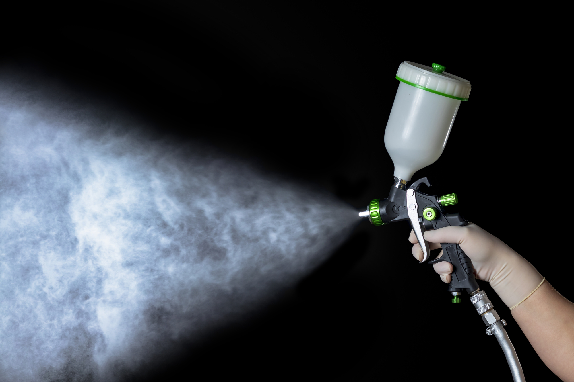 Fotografia de uma pessoa apertando o gatilho de uma pistola pulverizadora. Como o fundo da imagem é preto, é possível identificar as partículas emitidas pelo equipamento.