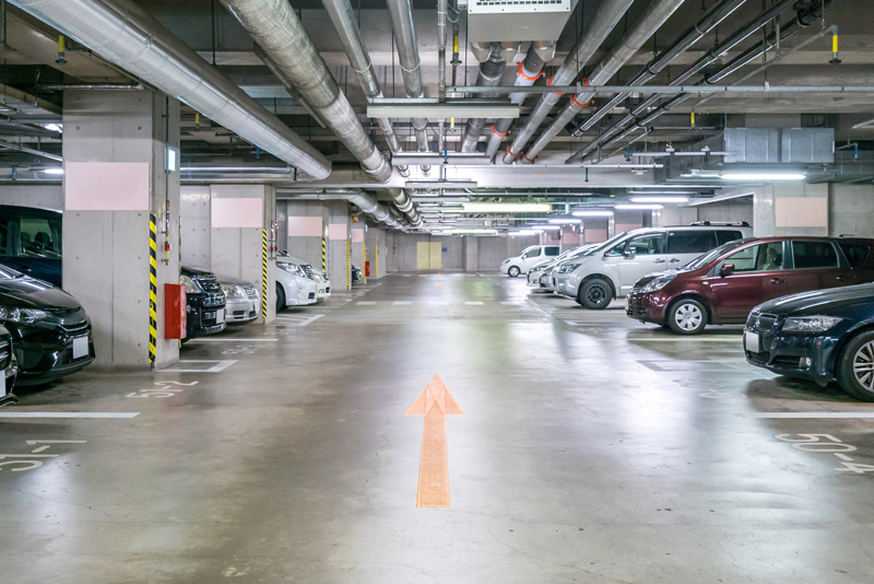 Fotografia de um estacionamento subterrâneo. Há diversos carros estacionados, e o piso é brilhante.