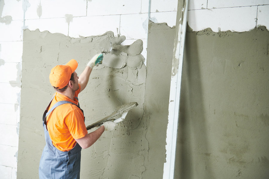 Fotografia de um homem rebocando uma parede de blocos de concreto.