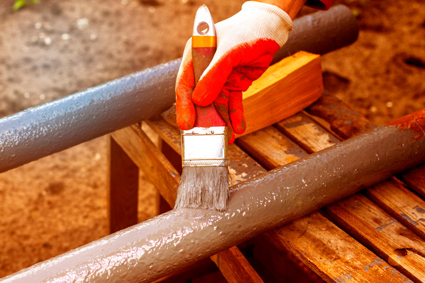 Fotografia de uma pessoa pintando um cano de PVC de marrom. Para isso, ela utiliza luvas e um pincel.