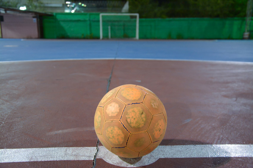 Fotografia de uma quadra esportiva. O piso está pintado e há uma trave, em uma das extremidades, e uma bola. 